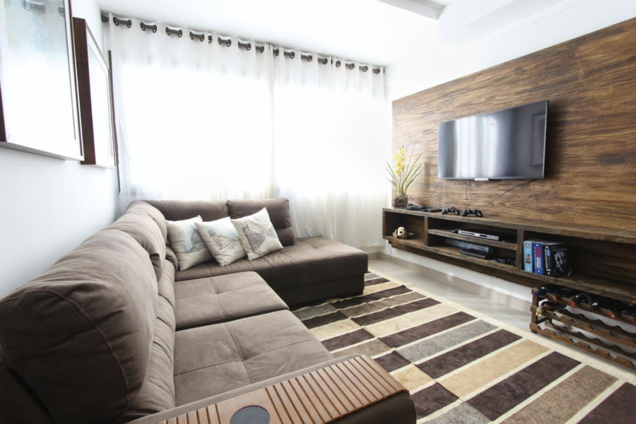 A modern living room featuring a brown sectional sofa, a TV wall-mounted on wood paneling, and a striped rug.